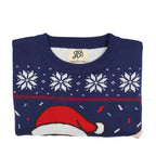 Folded navy blue ugly Christmas sweater with white snowflakes, red accents, and a Santa hat on a white background.