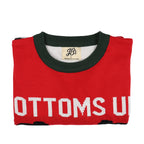 Folded red ugly christmas sweater with green neckline and 'Bottoms Up' text on a white background